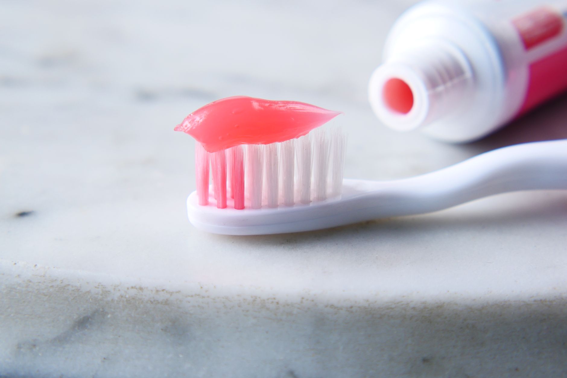 Close-up of a white toothbrush with red toothpaste against a white surface, highlighting dental care essential