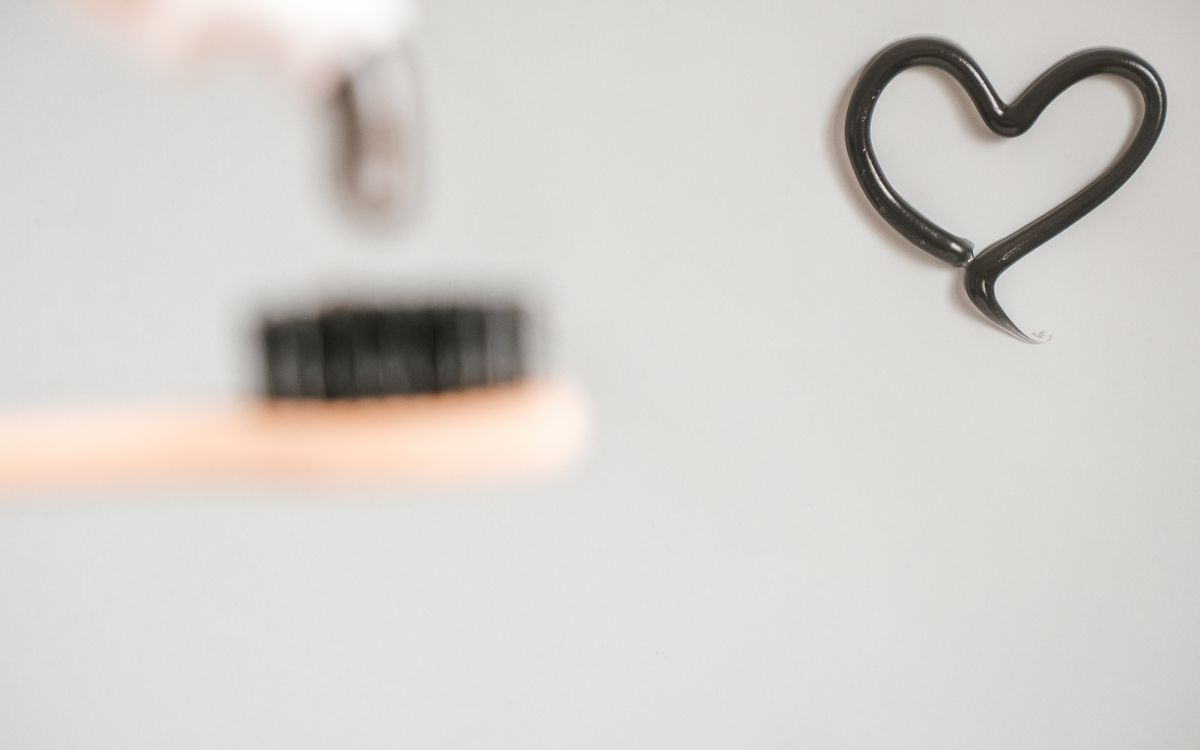 Minimalist image of a toothbrush and black toothpaste forming a heart shape on a white background.