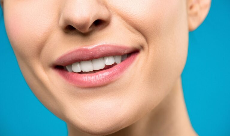 A close-up image of a womans smile with pink lipstick and white teeth against a blue background.