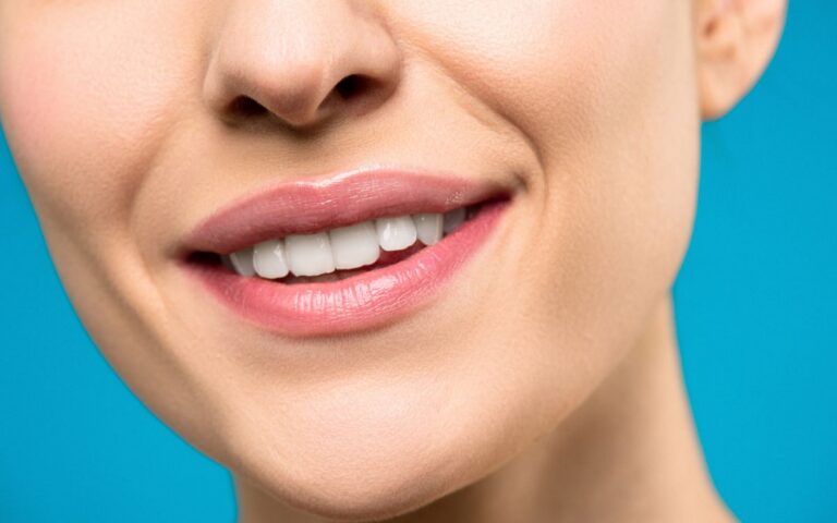 A close-up image of a woman's smile with pink lipstick and white teeth against a blue background.