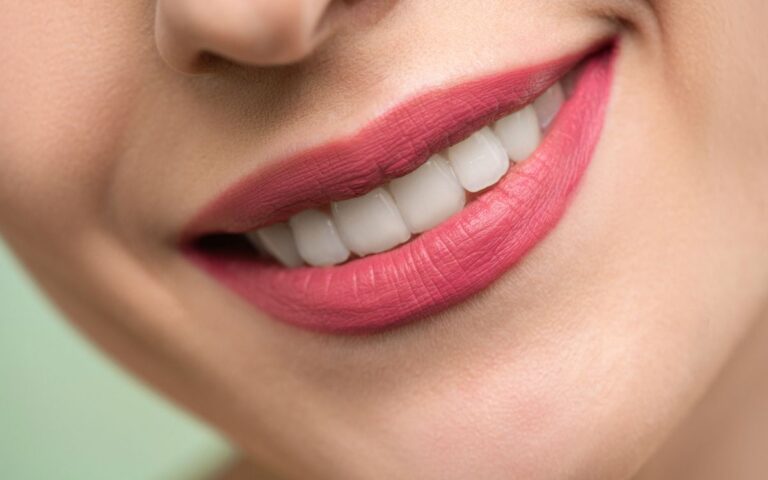 Vivid close-up image of a woman's smile showcasing red lipstick and white teeth on a light background.