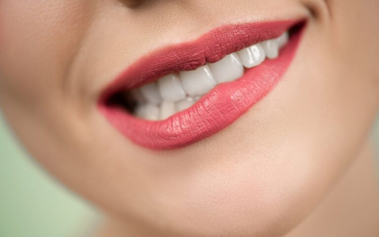 Close-up shot of woman's mouth wearing red lipstick, highlighting bright teeth and smooth skin.