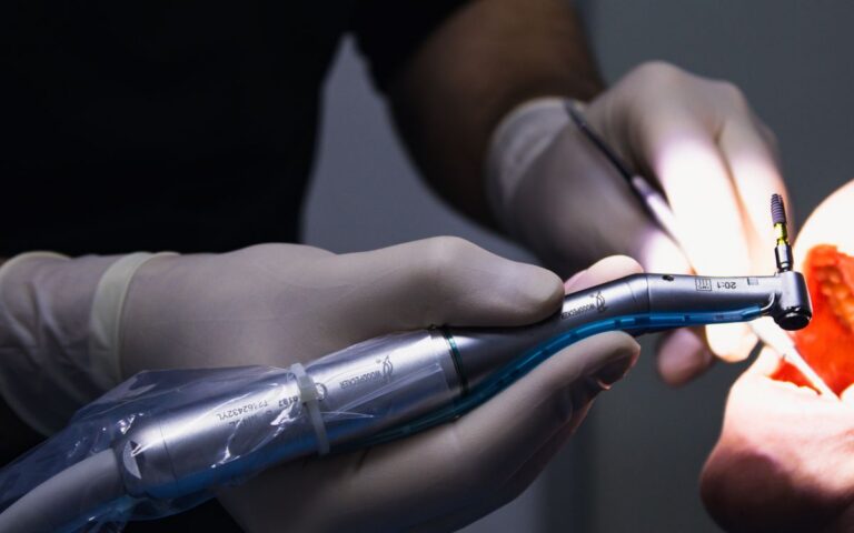 Detail of a dental procedure showing dentist using drill tool in patient's mouth.