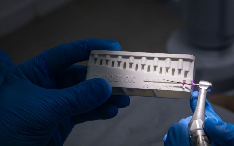 Close-up of dental tools and endoblock held by gloved hands in a clinic setting.