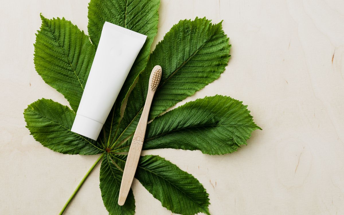 Overhead view of white mockup tube of organic toothpaste and eco friendly bamboo toothbrush placed flat on big green che