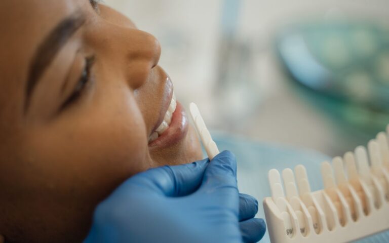 Smiling woman receiving a dental checkup with shade guide in the clinic.
