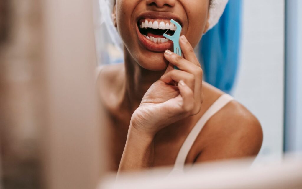 Mirror reflection of crop anonymous African American female with towel on head cleaning teeth with dental flosser in bat