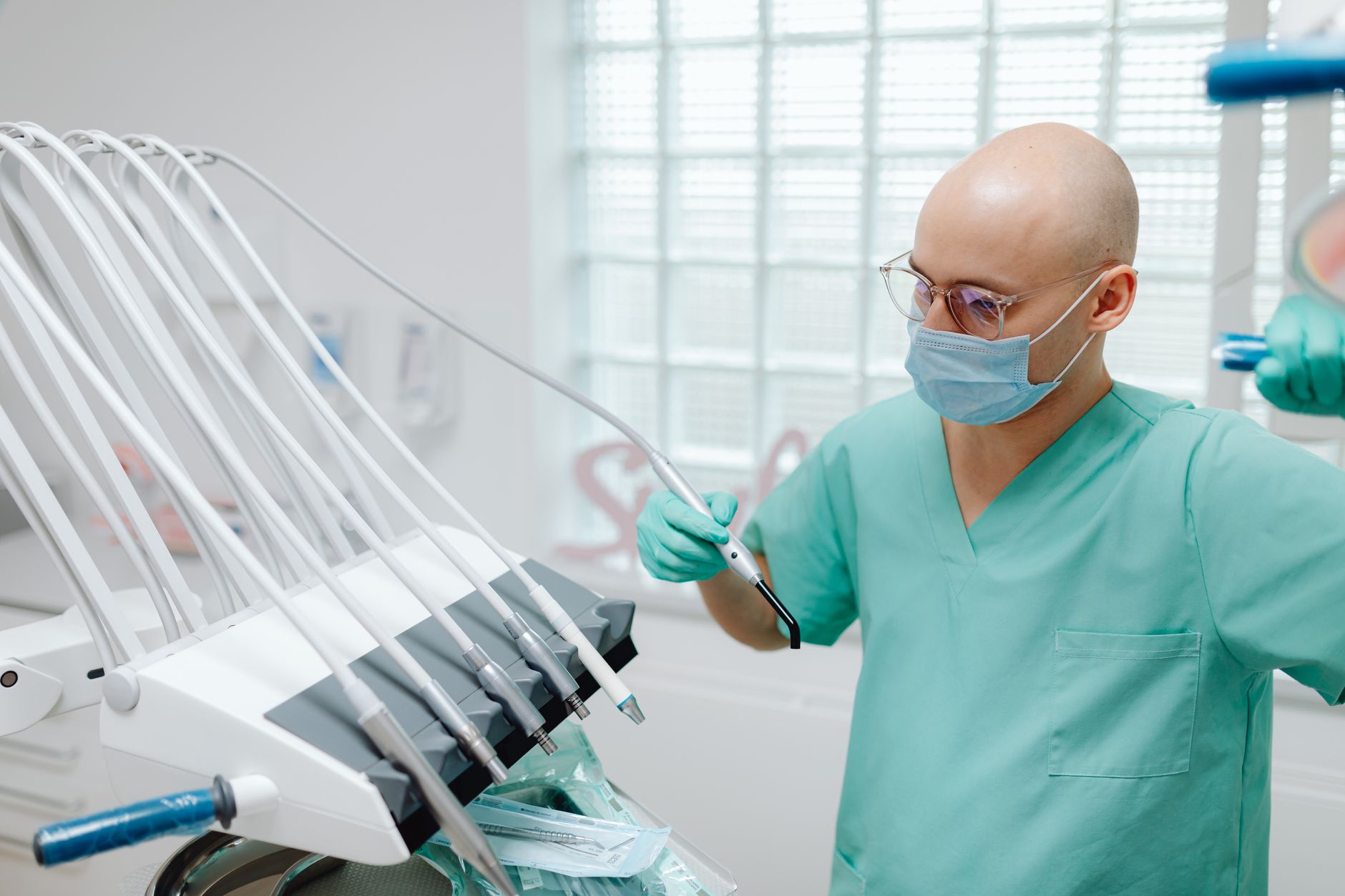 Dentist wearing mask and scrubs using dental instruments in a sterile clinic.