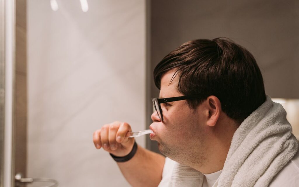 Side view of a man brushing teeth in bathroom, promoting daily dental care and hygiene.