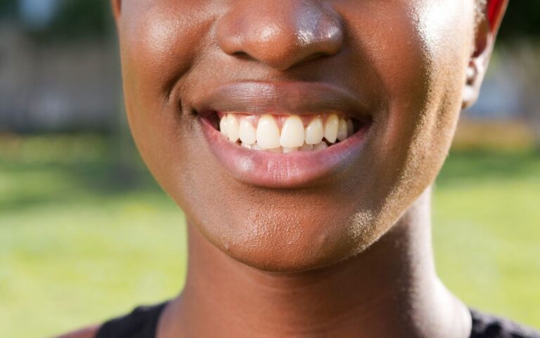 A close-up of a person smiling, showcasing their teeth and lips, captured outdoors.