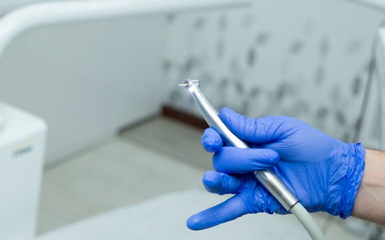 Close-up of a dentist's gloved hand holding a dental drill in a modern clinic setting.