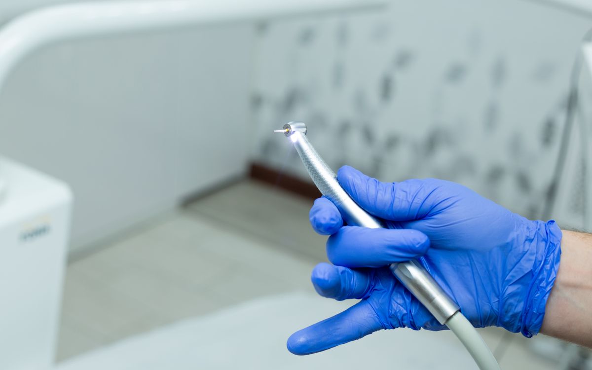 Close-up of a dentist's gloved hand holding a dental drill in a modern clinic setting.