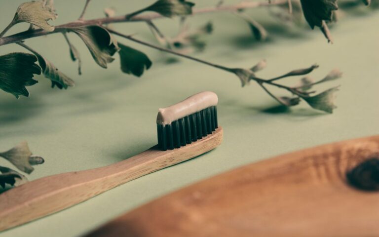 Wooden toothbrush with toothpaste on greenery background, promoting eco-friendly dental hygiene.
