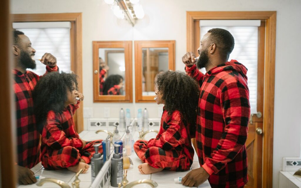 Father and daughter in matching pajamas brushing teeth together in a cozy bathroom.