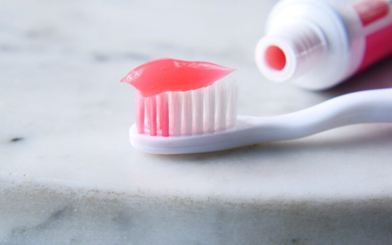 Close-up of a white toothbrush with red toothpaste against a white surface, highlighting dental care essentials.