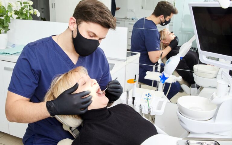 A dentist in a protective mask performing a dental procedure on a patient in a bright clinic.