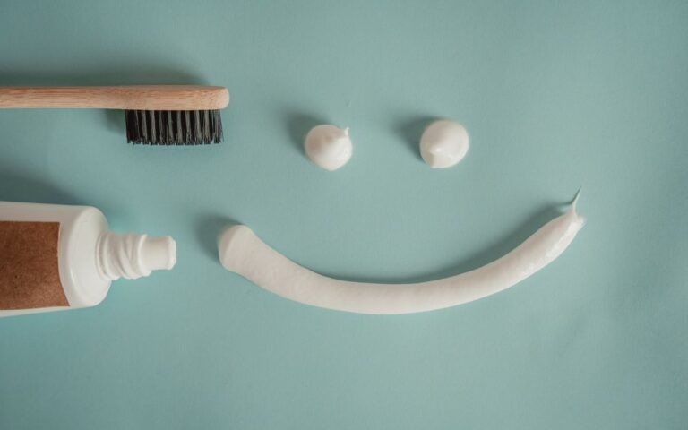 A playful arrangement of toothpaste and toothbrush forming a smile on a blue background.