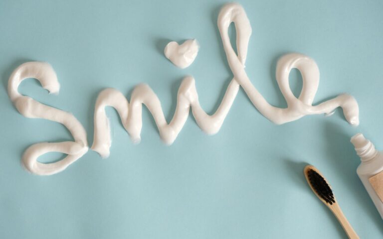 Toothpaste spelling 'Smile' on turquoise surface with toothbrush.