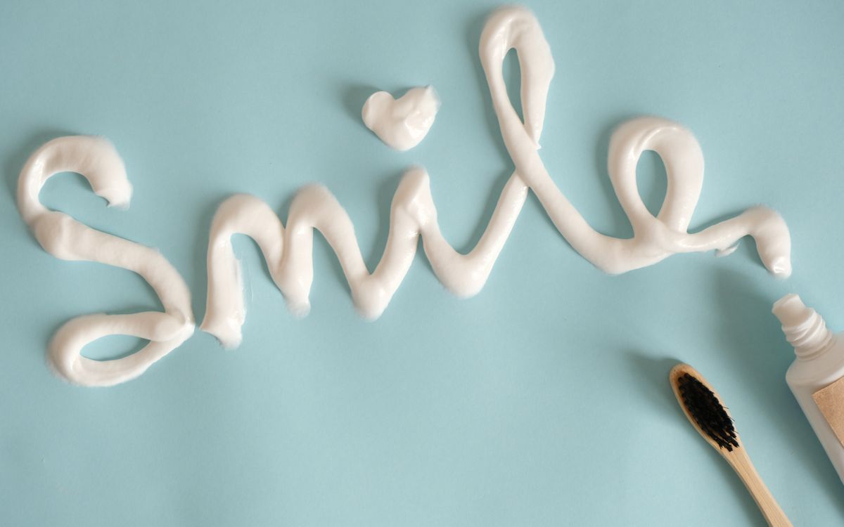Toothpaste spelling 'Smile' on turquoise surface with toothbrush.
