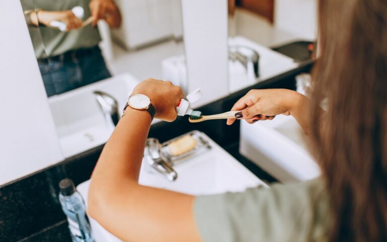 A woman is applying toothpaste to a toothbrush in a bathroom setting, showing daily oral hygiene habits.