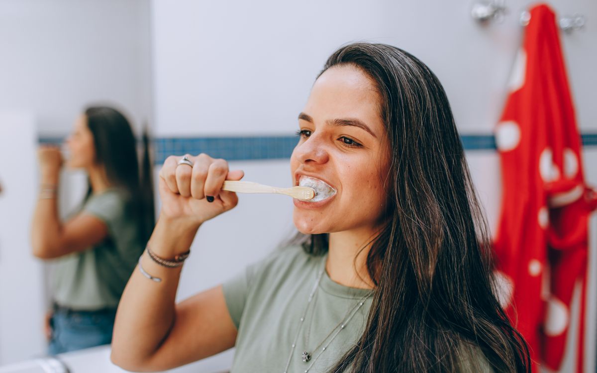 Young woman brushing teeth with toothbrush in a modern, bright bathroom. Focus on oral health care and hygiene.