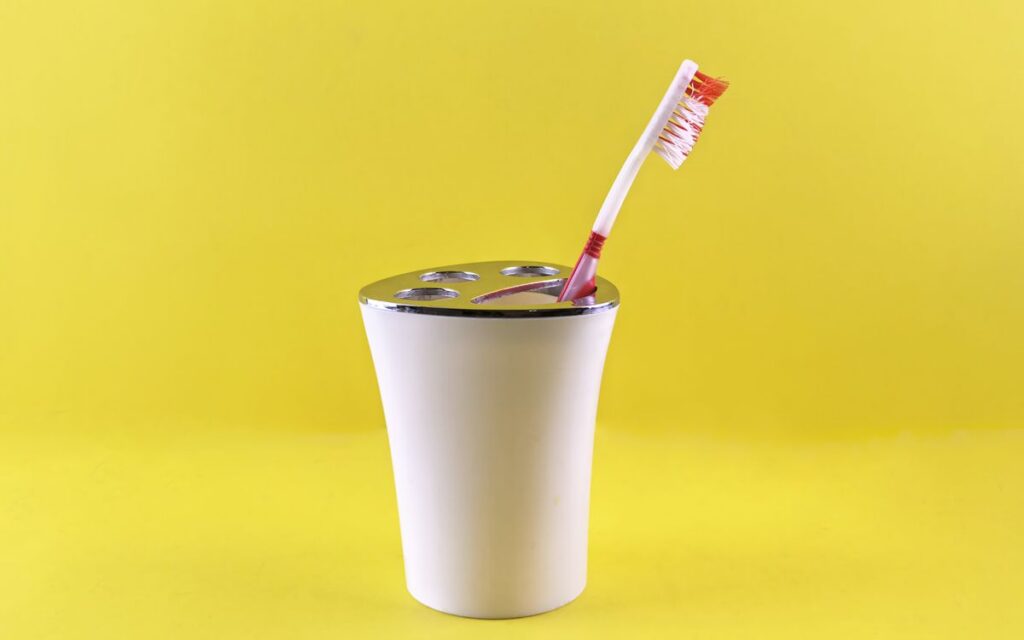 A red and white toothbrush in a white holder against a vibrant yellow background, showcasing dental hygiene.