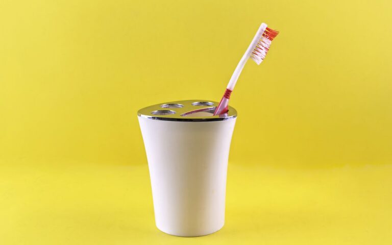 A red and white toothbrush in a white holder against a vibrant yellow background, showcasing dental hygiene.