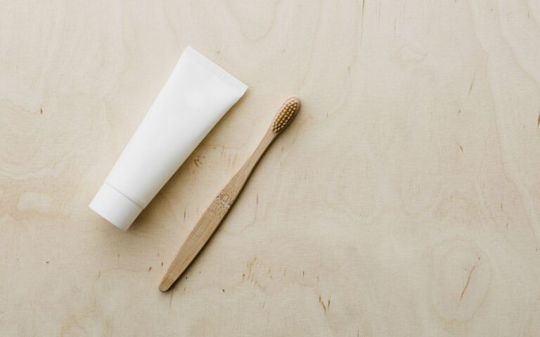 Overhead view of white mockup toothpaste tube and light brown bamboo toothbrush placed on wooden copy space surface