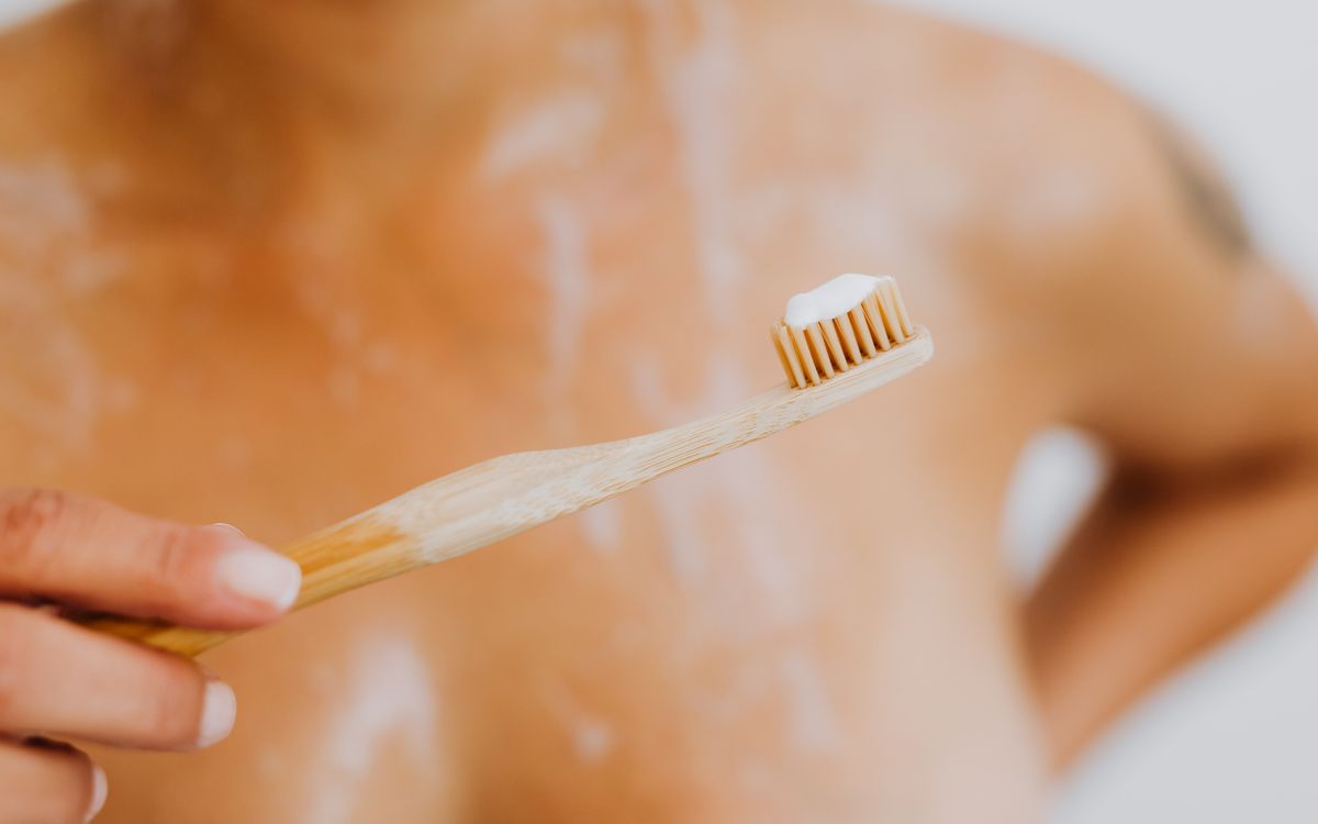 Close-up of a bamboo toothbrush held by a woman, emphasizing eco-friendly hygiene.