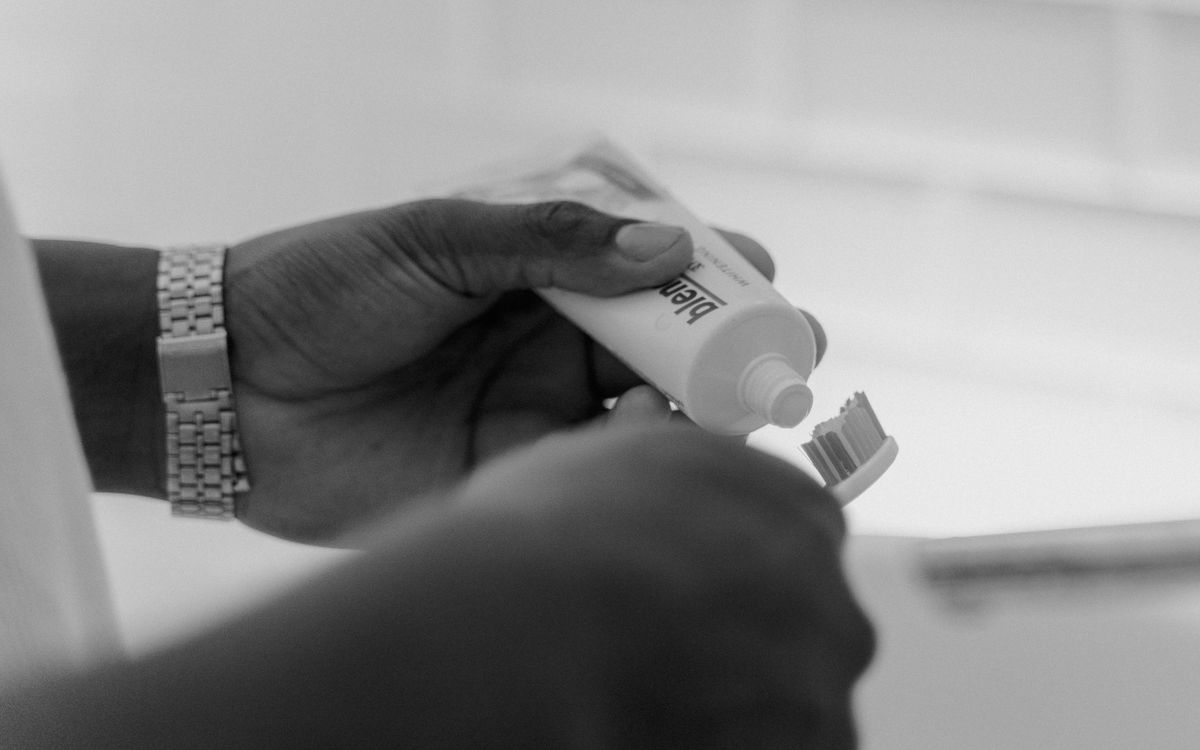 Monochrome close-up of hands applying toothpaste onto a toothbrush.
