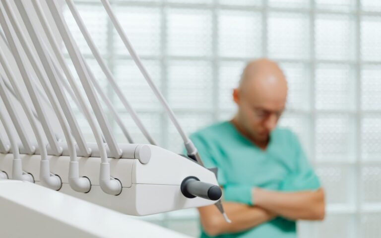 Close-up of dental tools with a blurred dentist in scrubs in the background.