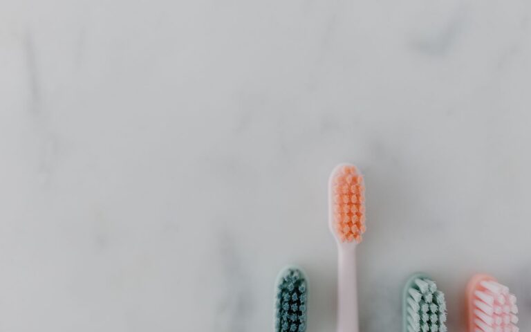 A clean and simple flat lay of four colorful toothbrushes on a marble surface.