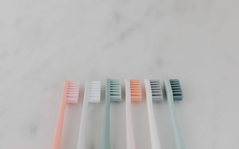 A row of colorful pastel toothbrushes aligned on a smooth marble surface.