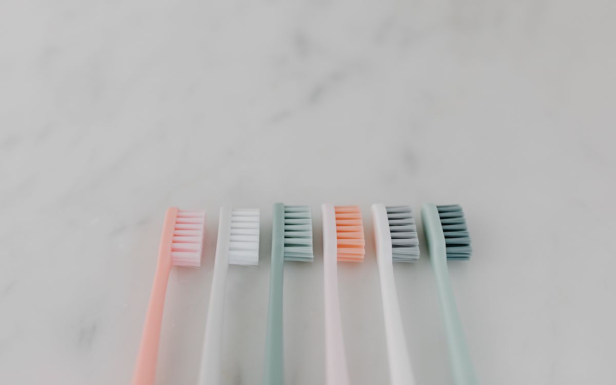 A row of colorful pastel toothbrushes aligned on a smooth marble surface.