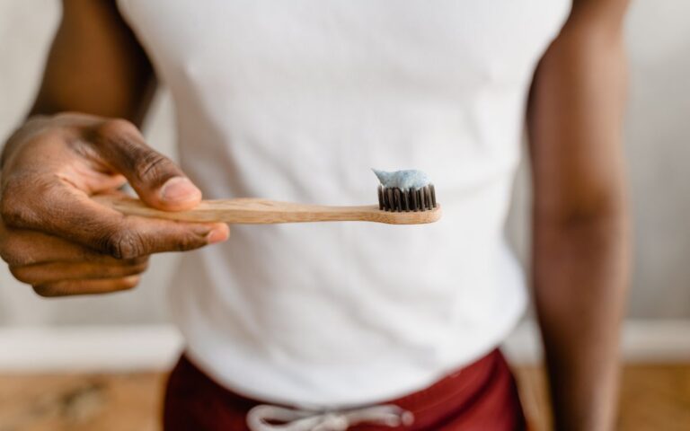 An adult holding a bamboo toothbrush with toothpaste, promoting eco-friendly dental care.