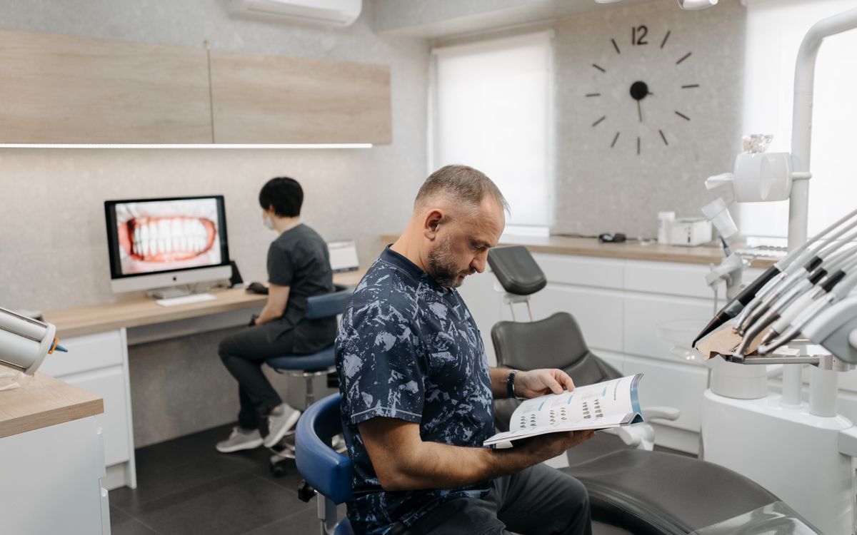 A dental professional reads a brochure while another works on a computer in a contemporary clinic.