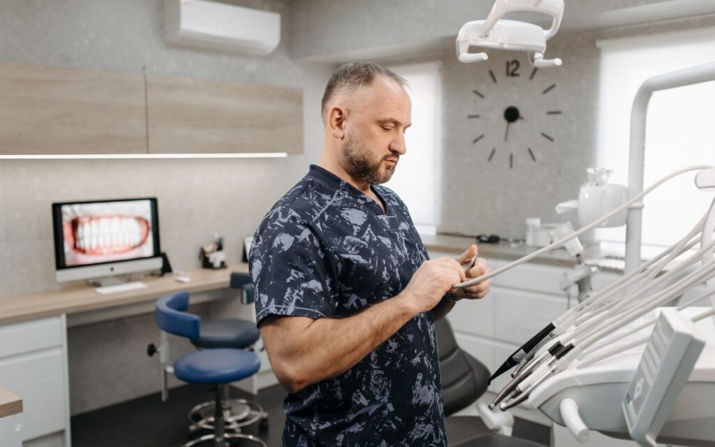 Dentist preparing dental tools in a modern dental office with equipment and patient images.