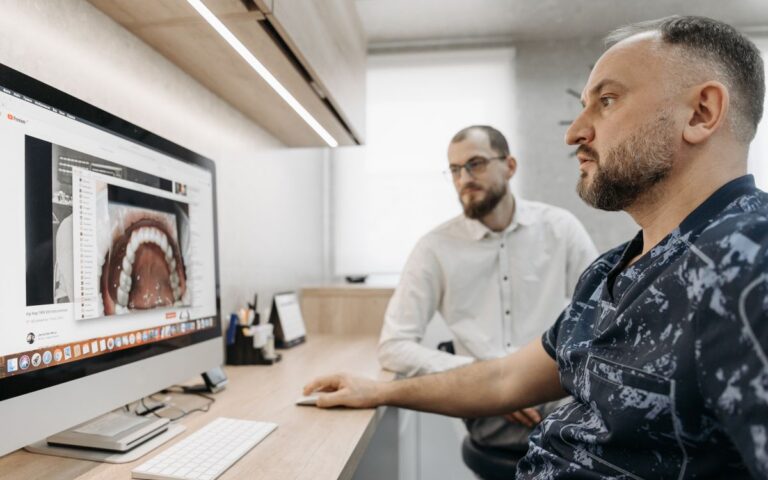 Two men discuss dental care at a computer, illustrating modern digital dentistry.