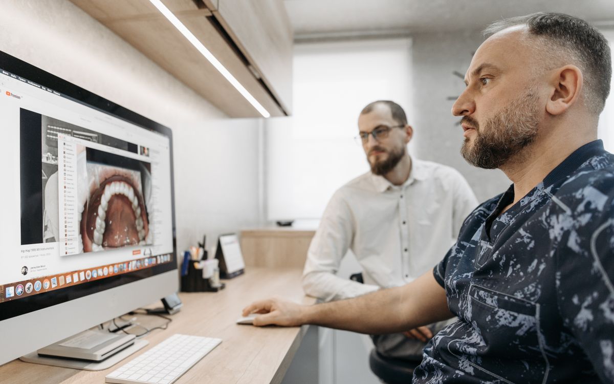 Two men discuss dental care at a computer, illustrating modern digital dentistry.