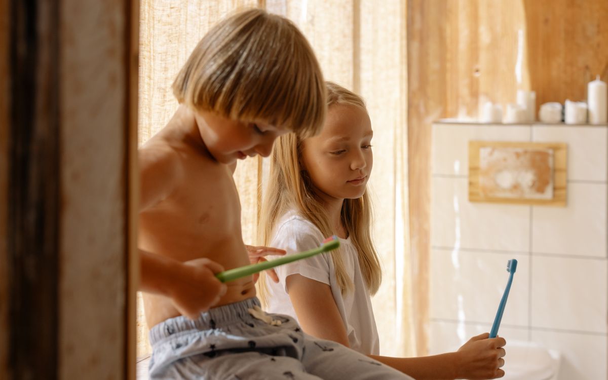 Two children brushing teeth together in a warm, sunlit bathroom promoting dental care.