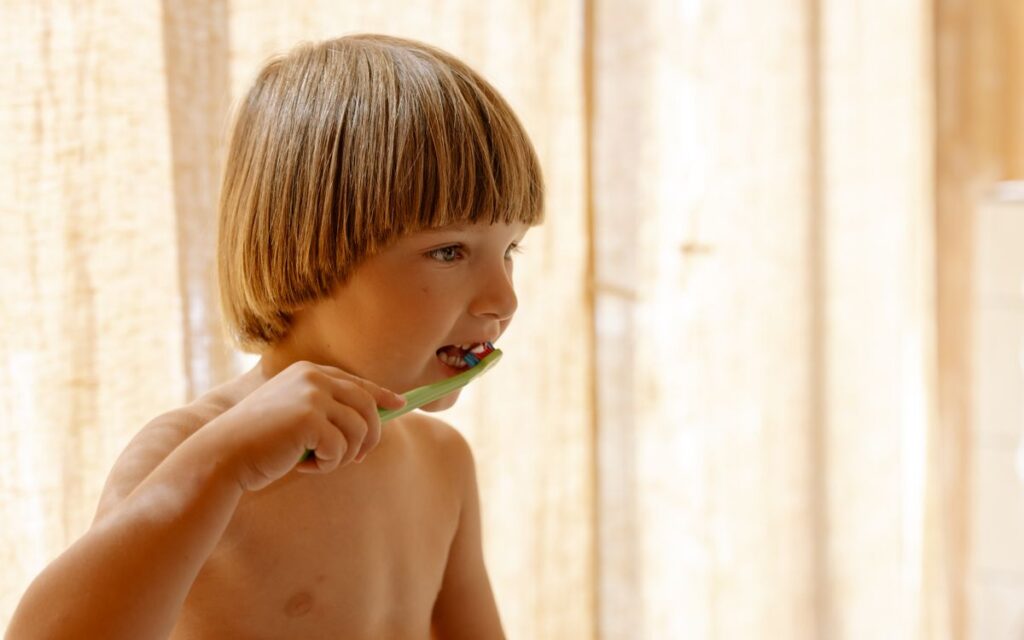 Young boy brushing teeth indoors in soft natural light, promoting dental care routines.