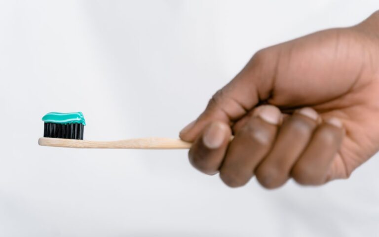 Hand holding a bamboo toothbrush with green toothpaste, focusing on oral hygiene.