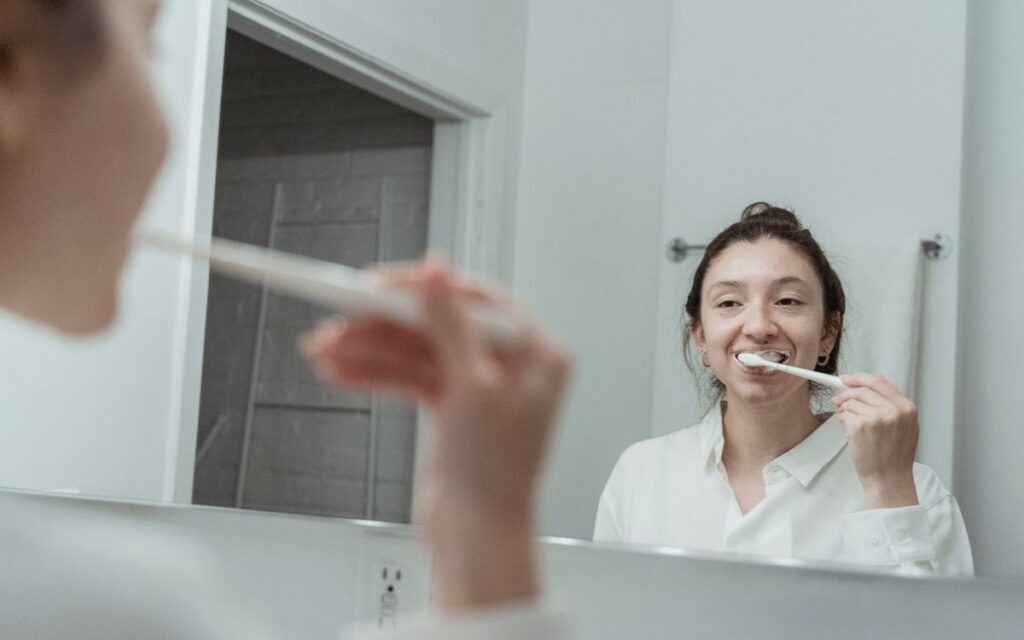 A woman with hair bun brushing her teeth in front of mirror, focusing on dental hygiene.