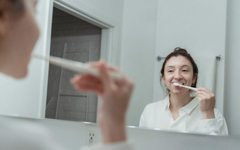 A woman with hair bun brushing her teeth in front of mirror, focusing on dental hygiene.