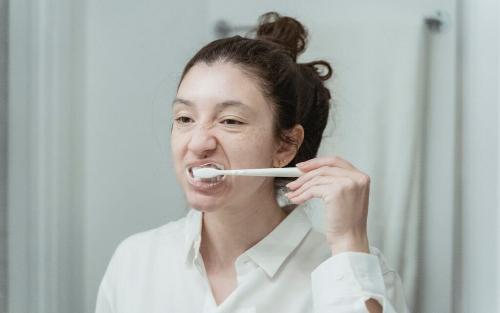 A young woman brushes her teeth in front of a bathroom mirror, focusing on oral hygiene.