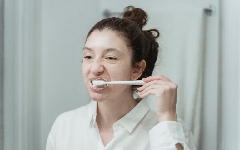 A young woman brushes her teeth in front of a bathroom mirror, focusing on oral hygiene.