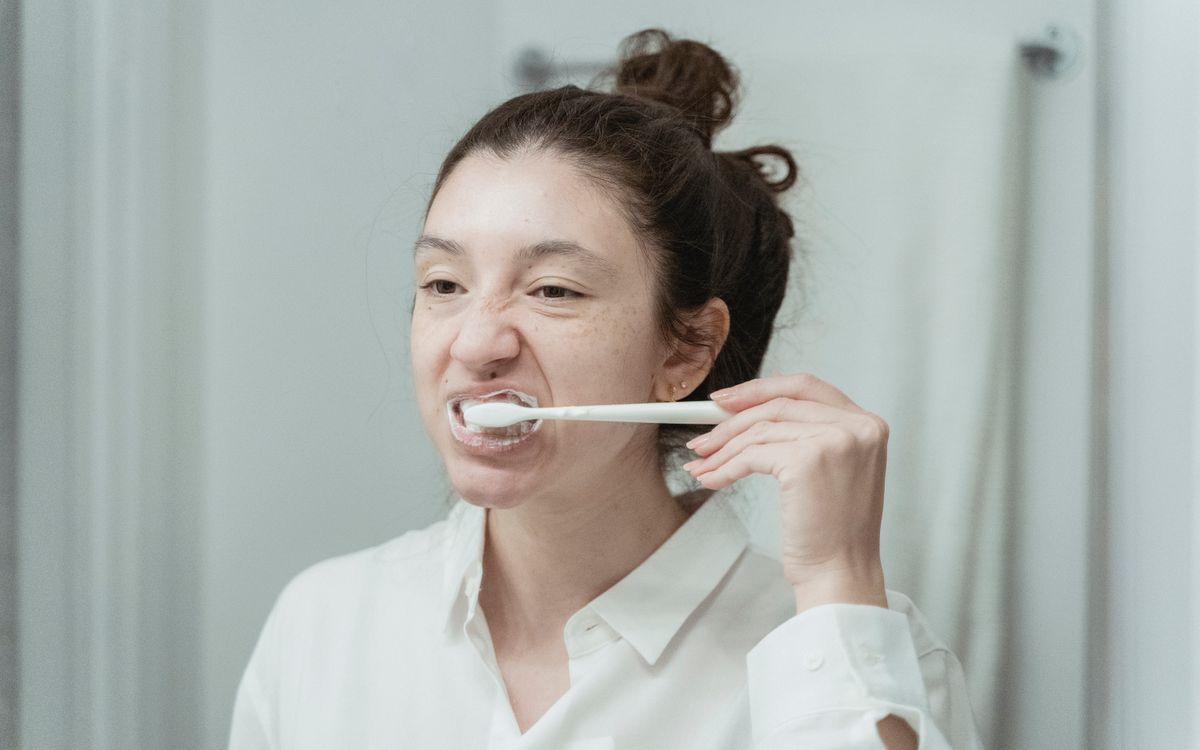 A young woman brushes her teeth in front of a bathroom mirror, focusing on oral hygiene.