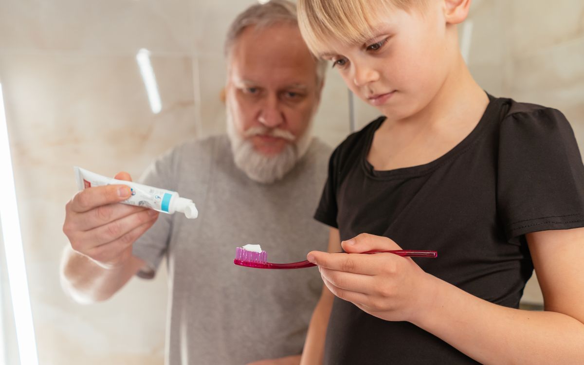 A grandfather assists his young grandson with dental hygiene in a bathroom setting.