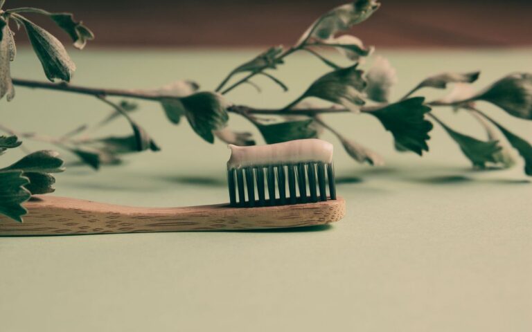 Wooden toothbrush with toothpaste against a plant background, emphasizing natural oral care.