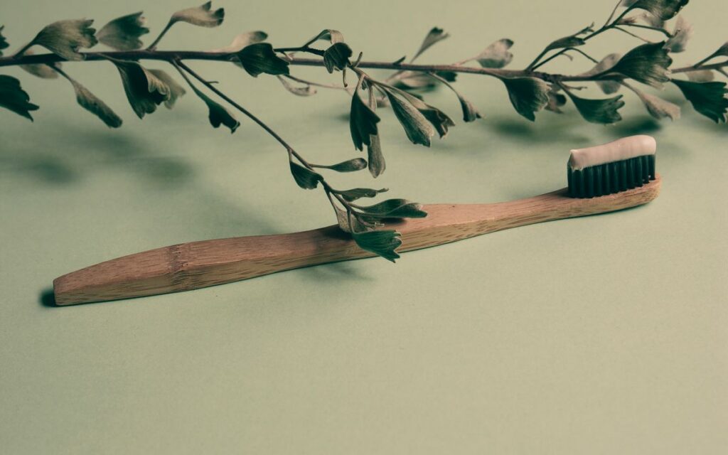 A bamboo toothbrush with toothpaste lies on a green background adorned with leaves, promoting natural oral care.
